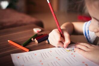 Little Girl writing on a worksheet with colored pencils.